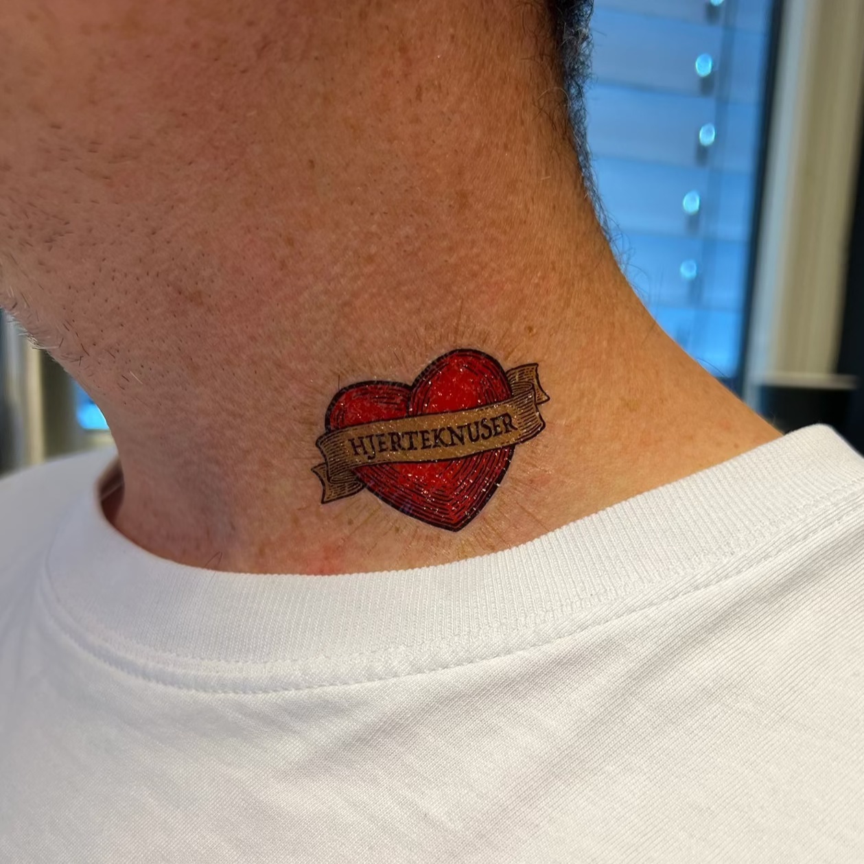 Heart-shaped tattoo on a person's neck with Kaizers Orchestra design